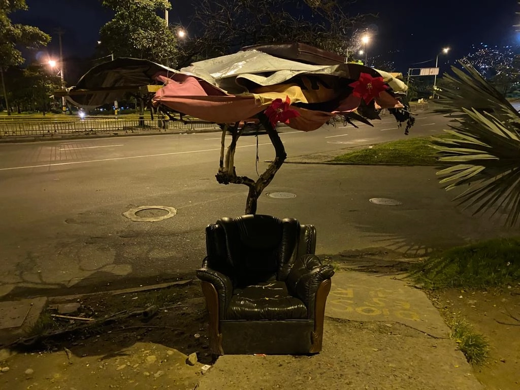 an image of a worn down couch seat with an umbrella made of variosu fabrics on a street in Colombia