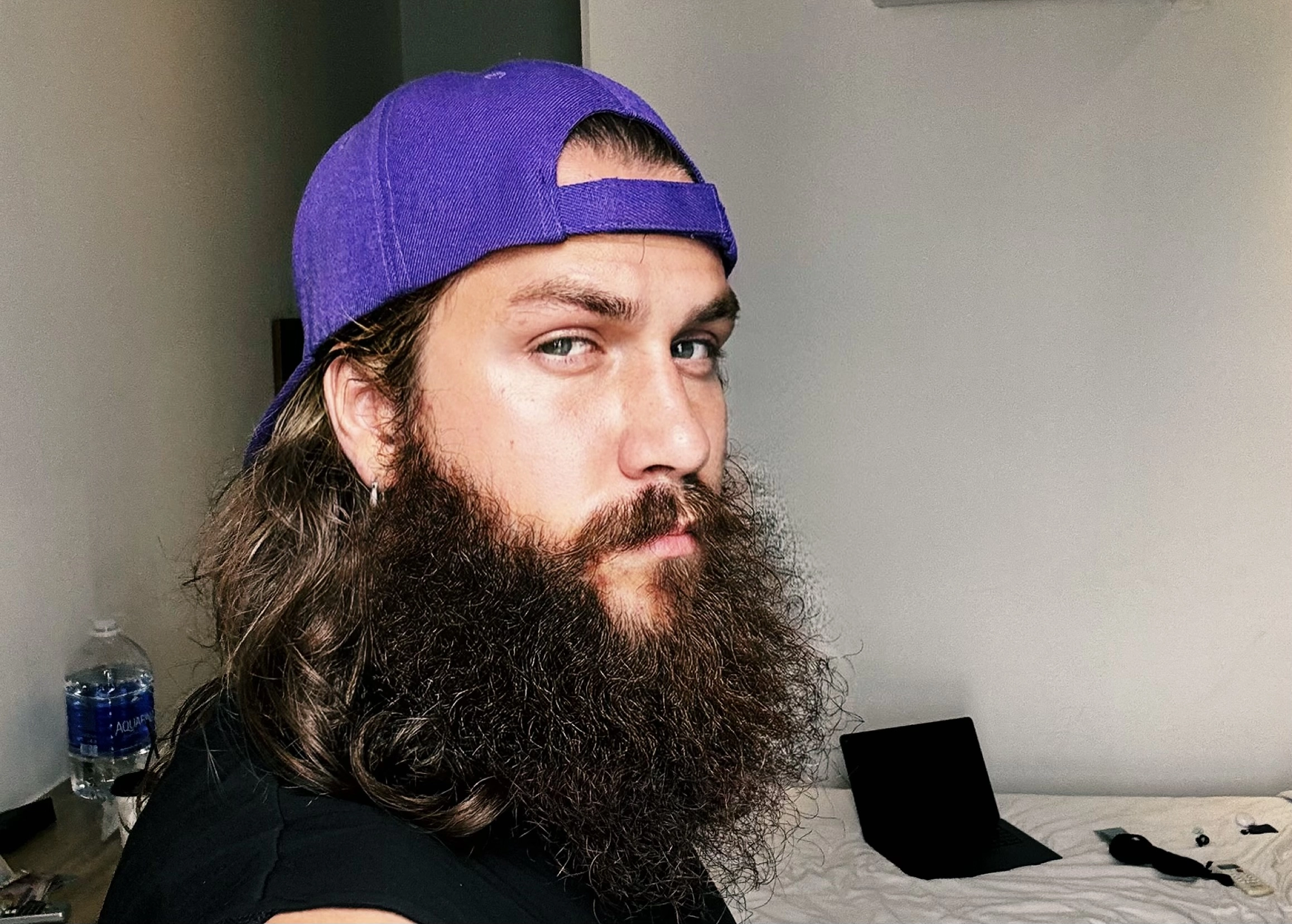 an image of a chad with a large beard, long hair and a purple baseball hat worn in reverse